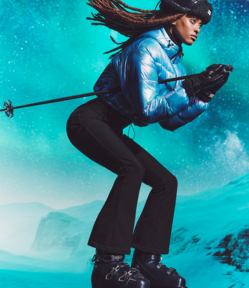 Dynamic winter fashion with DKNY Tech's reflective blue ski jacket and black pants, ready for a downhill adventure.