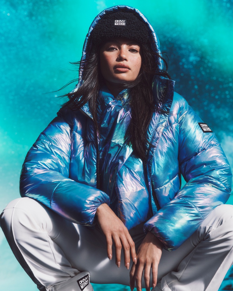 Apres-ski allure: Kelsey Merritt sits in a metallic blue puffer jacket and knit beanie, complemented by pristine white ski pants.