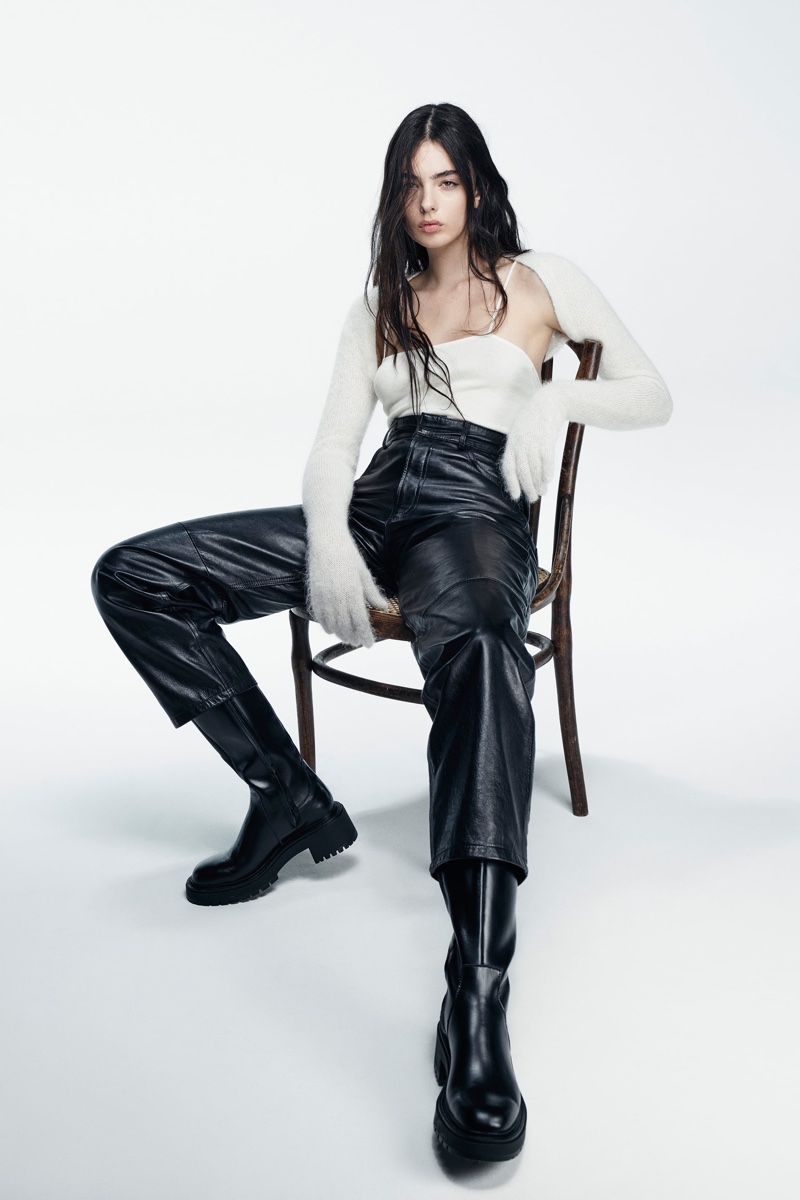 Effortlessly cool, Deva Cassel sits casually in a cream knit top and sleek leather trousers, highlighting Zara's versatile winter pieces.