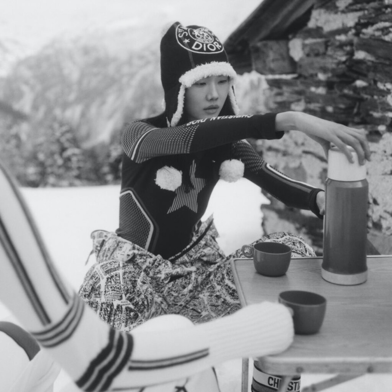 Sijia Kang pours a warm beverage, wearing a cozy Dior knit hat, showcasing a laid-back moment in the DiorAlps 2023 collection.