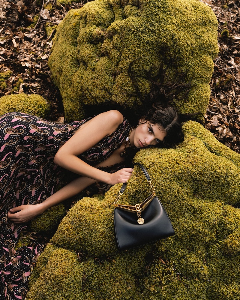 Sun Mizrahi lounges on a moss-covered rock, her gaze introspective, clutching an elegant Etro handbag for the brand's winter 2023 campaign.