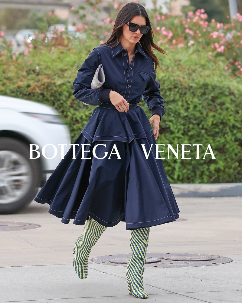 Kendall Jenner showcases Bottega Veneta's pre-spring 2024 collection with a navy blue A-line dress and striped green knee-high boots.
