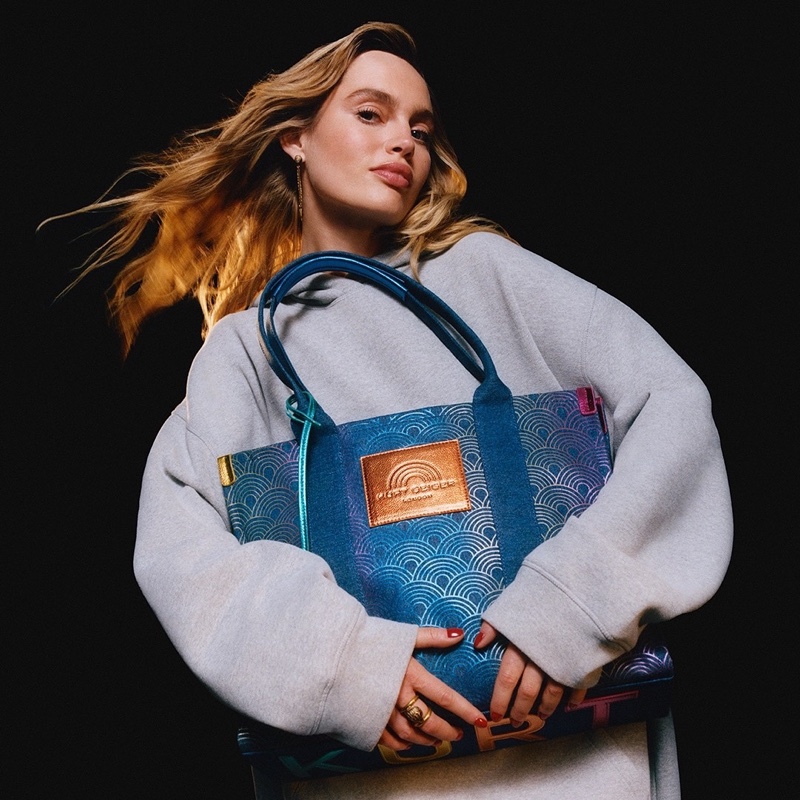 Staz Lindes clutches a vibrant Kurt Geiger Southbank tote against a cozy grey sweatshirt for the brand's holiday 2023 campaign.