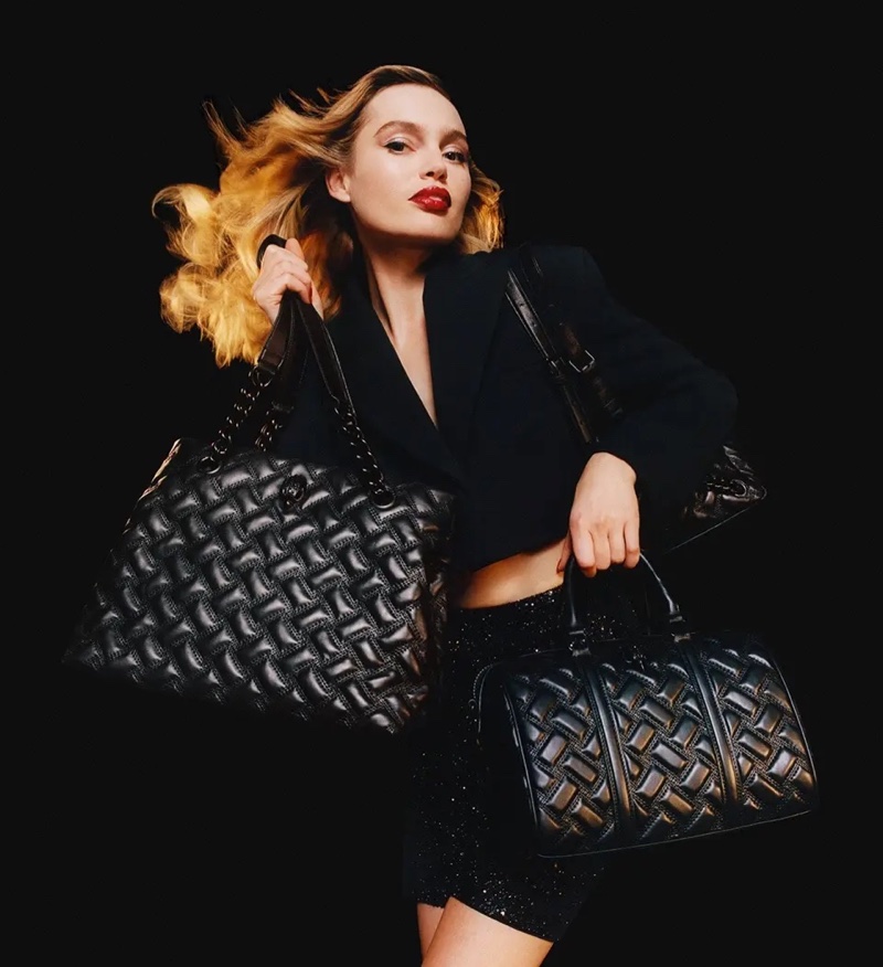 Staz Lindes strikes a dynamic pose, her hair flowing, while showcasing two Kurt Geiger bags, a juxtaposition of movement and style for the holiday season.