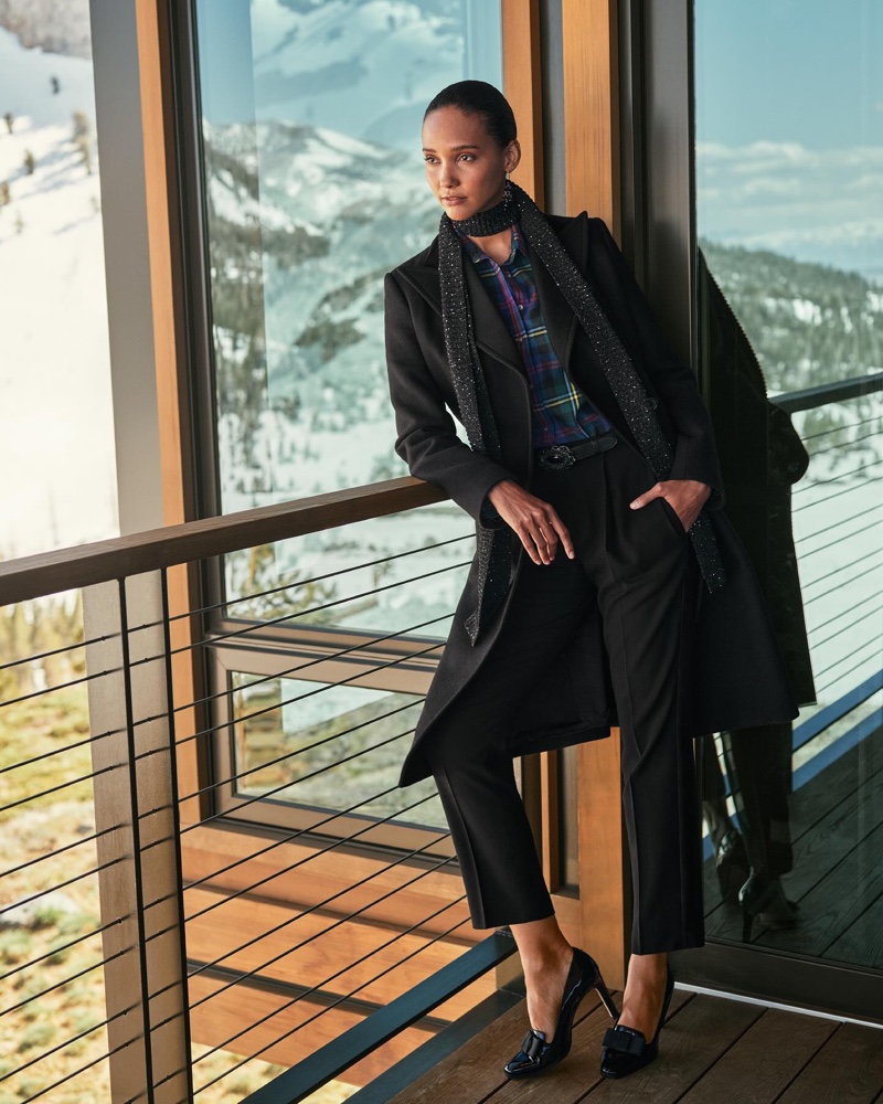 Refined relaxation overlooking snowy peaks: Lauren Ralph Lauren showcases a layered winter look with a shimmering scarf, black coat, and plaid accents.