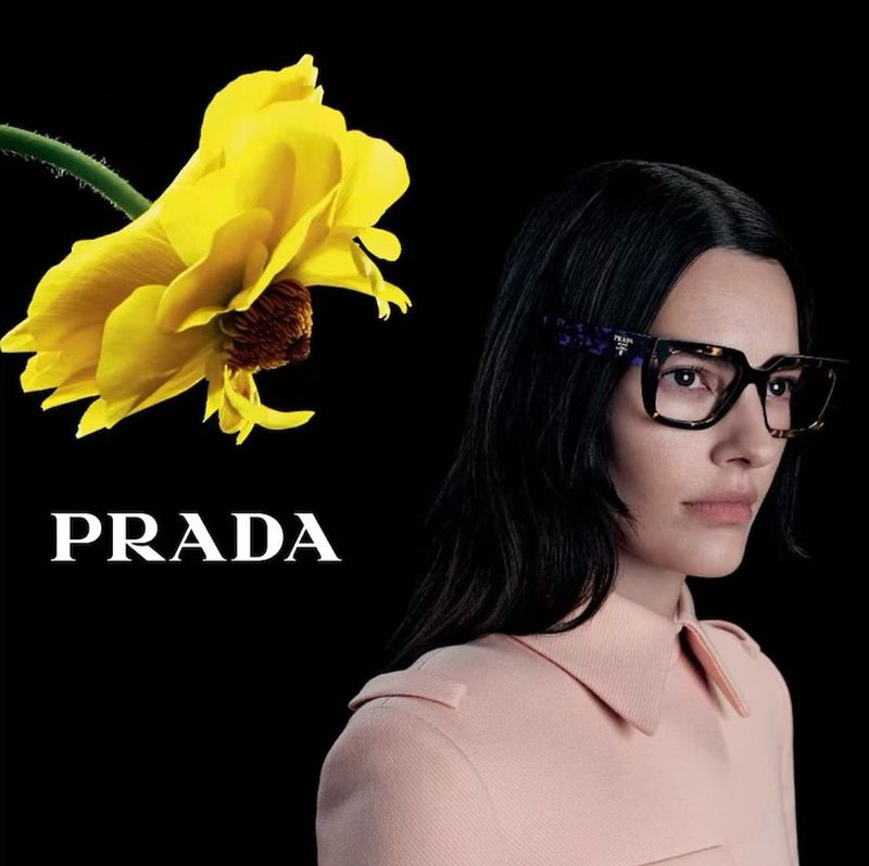 In pastel attire, Amanda Murphy is complemented by chic eyeglasses and a bold yellow flower in Prada eyewear's fall-winter 2023 campaign.