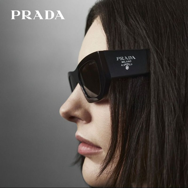 Profile view of Prada sunglasses with bold branding on the temples, set against a minimalist grey backdrop for the winter 2023 eyewear campaign.