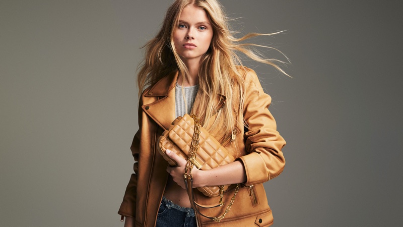 Evie Harris clasps a caramel Tribeca bag, complementing her tan leather jacket in the Michael Kors campaign.