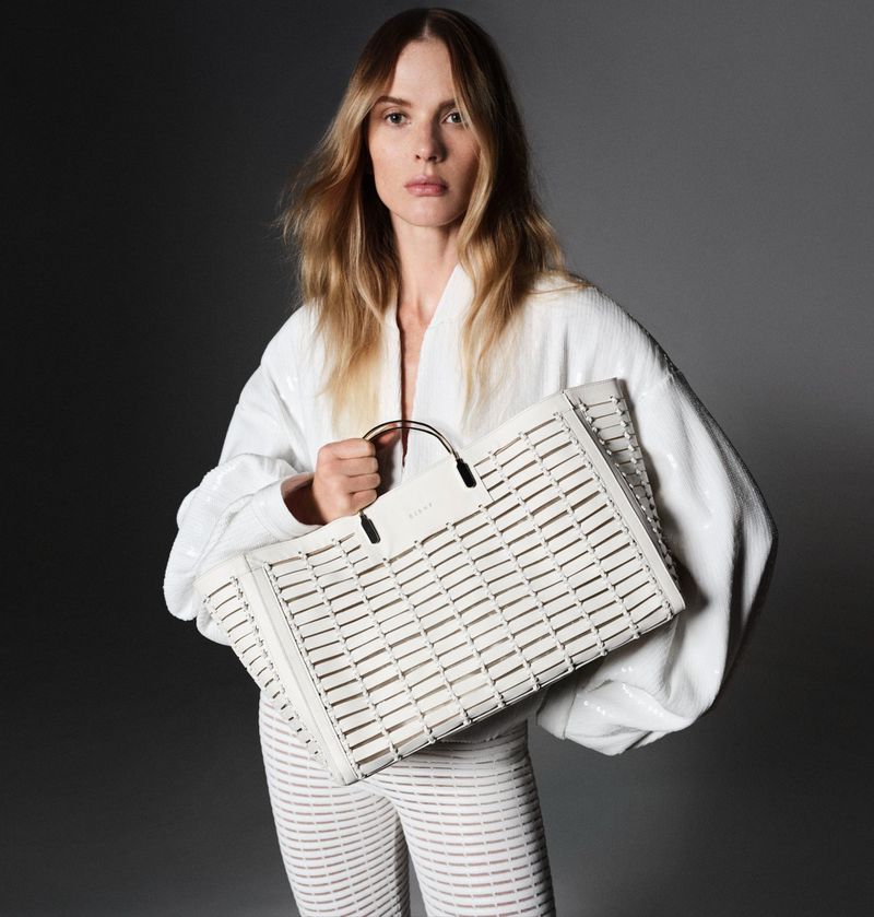 Anne Vyalitsyna showcases a white textured blouse and trousers, clutching a large woven tote for Genny's spring 2024 campaign.