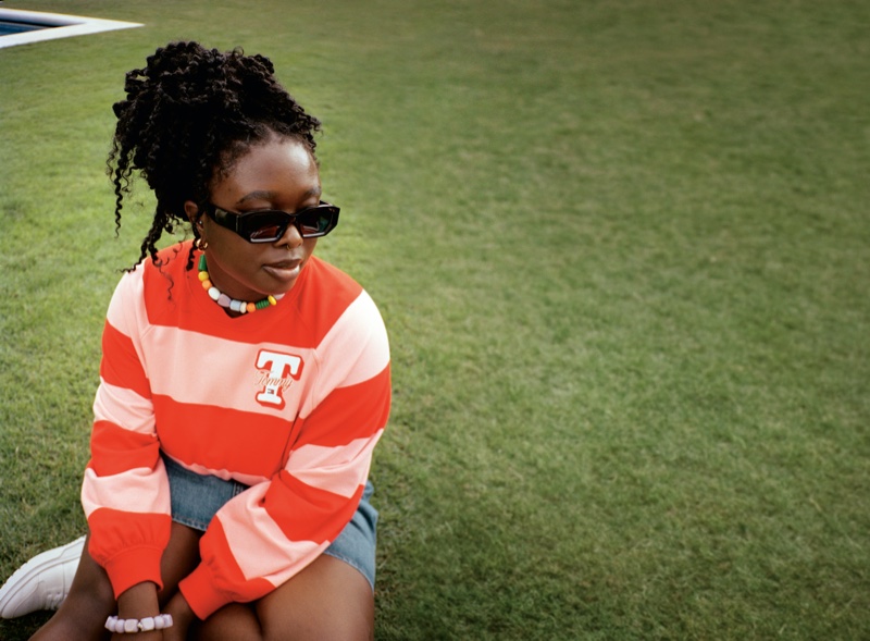 Relaxed in striped orange knit, a model showcases Tommy Jeans' casual spring 2024 look.