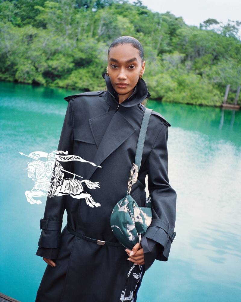 Chey Carty shows off a structured black trench coat and printed bag for the Burberry summer 2024 ad.