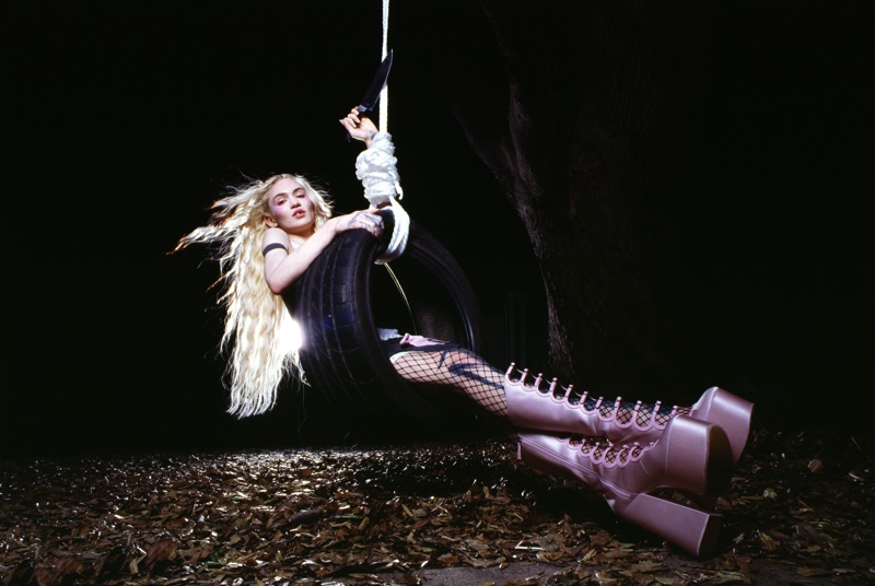 Grimes swings on a tire in the night, showcasing chunky lavender boots for Heaven by Marc Jacobs spring 2024 ad.