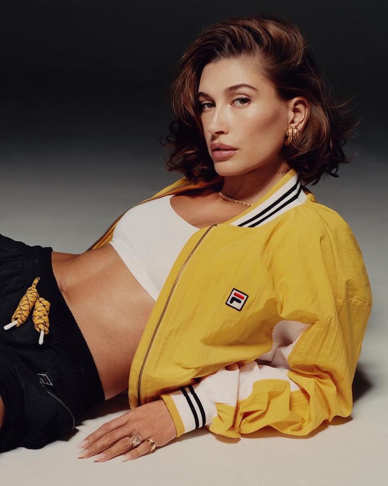 Model Hailey Bieber showcases vibrant energy in a yellow Settanta jacket and white top for FILA's new advertisement. 