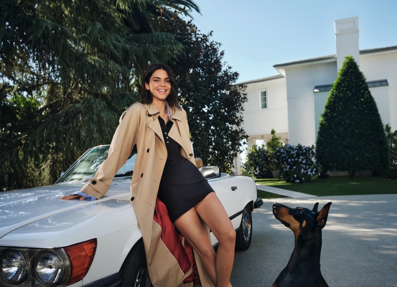 Kendall Jenner radiates chic vibes, leaning on a classic car, adorned in a beige trench coat for Tommy Hilfiger spring 2024.