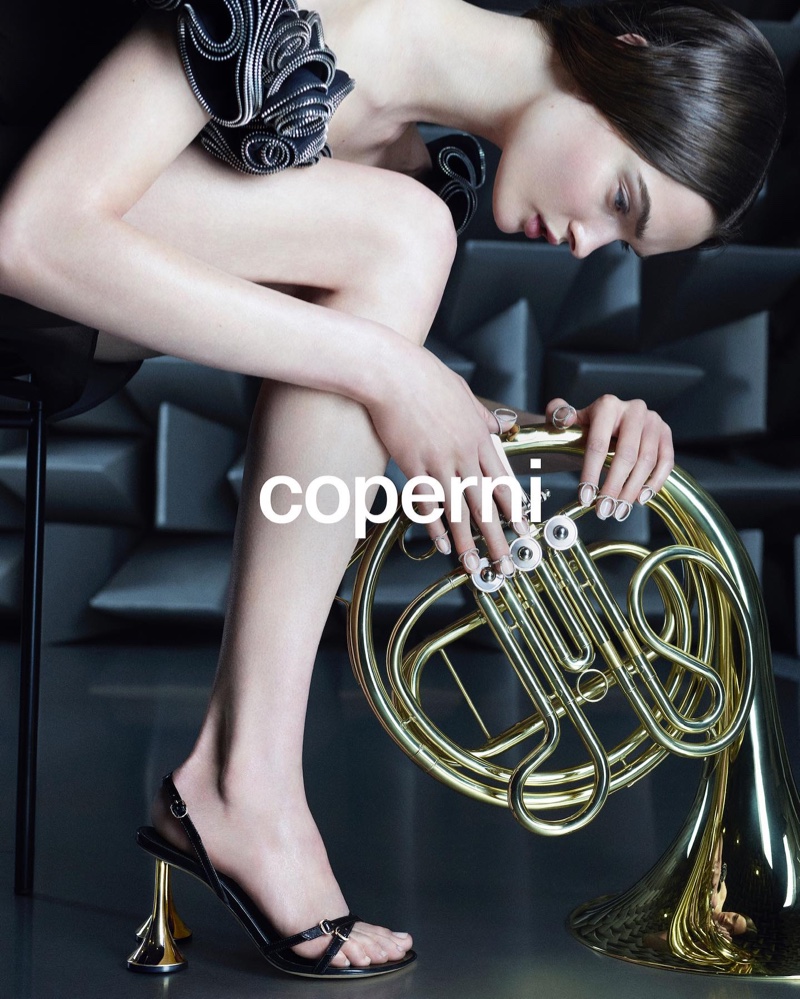 Lulu Tenney poses with Coperni's spring 2024 collection and a French horn.